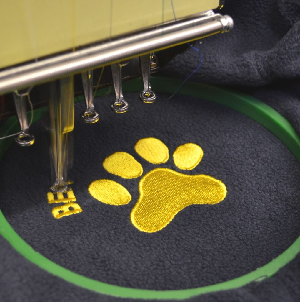A pawprint logo being embroidered on to clothing by a machine